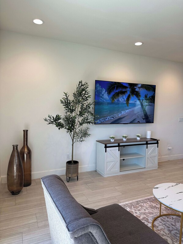 Una sala de estar con un televisor de pantalla plana montado en la pared, un sofá gris, una mesita redonda y una planta decorativa.