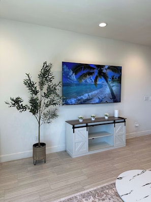 A living room with a large flat-screen TV mounted on the wall, a white entertainment unit with shelves, a potted plant, and a patterned rug. - Private 3BR Townhouse Near Disneyland & Knott’s (Garden Grove)