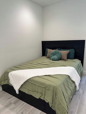 Una cama con un edredón verde, una manta blanca y varias almohadas.