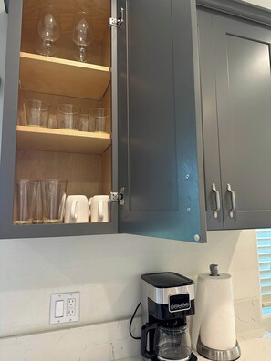 A kitchen with a coffee maker, a paper towel dispenser, and a cabinet with wine glasses and cups. - 3BR Townhouse for Groups, Near Disneyland (Garden Grove)