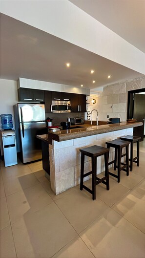 A modern kitchen with a central island, bar stools, stainless steel appliances, and a water dispenser. - Aldea Thai PH - Private Oceanfront Pool - Entire condo in Playa del Carmen (Playa del Carmen)