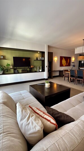 Un salon moderne avec un grand canapé, une table basse et un téléviseur à écran plat. Il y a également un coin repas avec une table et des chaises.