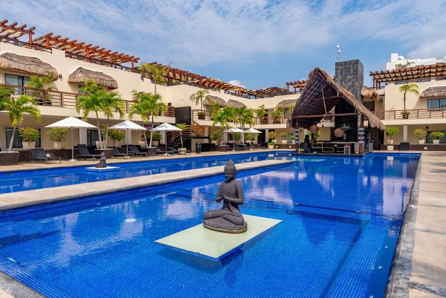 Ein Swimmingpool mit einer Buddha-Statue in der Mitte, umgeben von Liegestühlen und Sonnenschirmen.