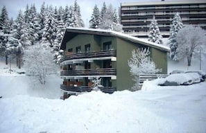 A multi-story building with balconies, surrounded by snow-covered trees and a parking area. - Balcony, tv, ski locker, 50m², Chamrousse (Chamrousse)