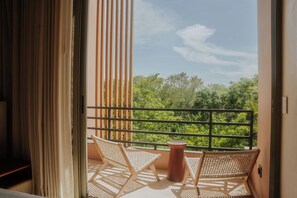 Un balcón con dos sillas de mimbre y una mesa de terracota, con vistas a un paisaje verde y exuberante.
