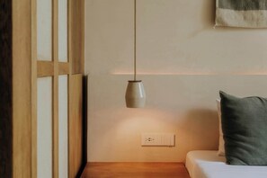 Ein Schlafzimmer mit einem Nachttisch aus Holz, einer Lampe, einer Steckdose und einem Bett mit Kissen.