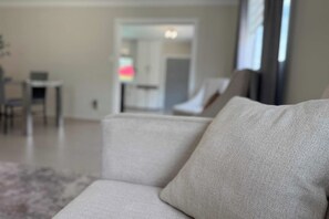 A modern living room with a sofa, a coffee table, and a dining area in the background.