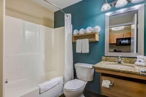 Et badeværelse med badekar, toilet, håndvask og et spejl over vasken.
