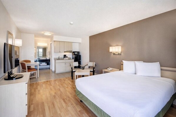 Habitación de hotel con cama, escritorio, sillas, televisión, microondas y kitchenette.