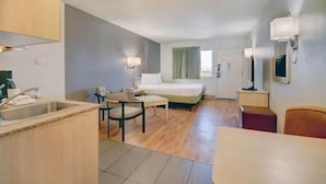 Ein kleines Hotelzimmer mit Küchenzeile, einem Bett, einem Schreibtisch und einem Stuhl.
