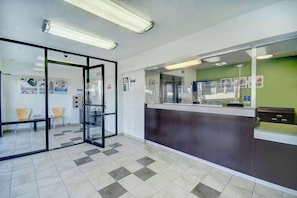 Zona de recepción con mostrador de check-in, puertas de cristal y suelo de baldosas.