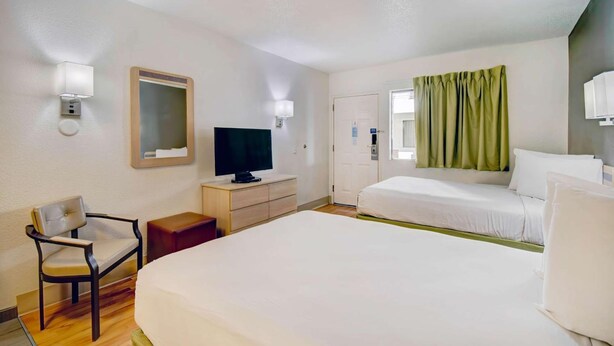 Ein Hotelzimmer mit einem Bett, einem Sessel, einem Fernseher, einem Schminktisch und einer Tür.