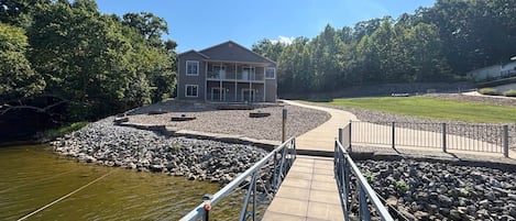 A two-story building with a balcony, a stone retaining wall, and a paved dock leading to a body of water.
