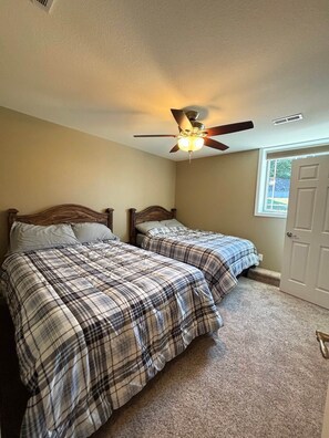 Quarto com duas camas, um ventilador de teto e uma janela.