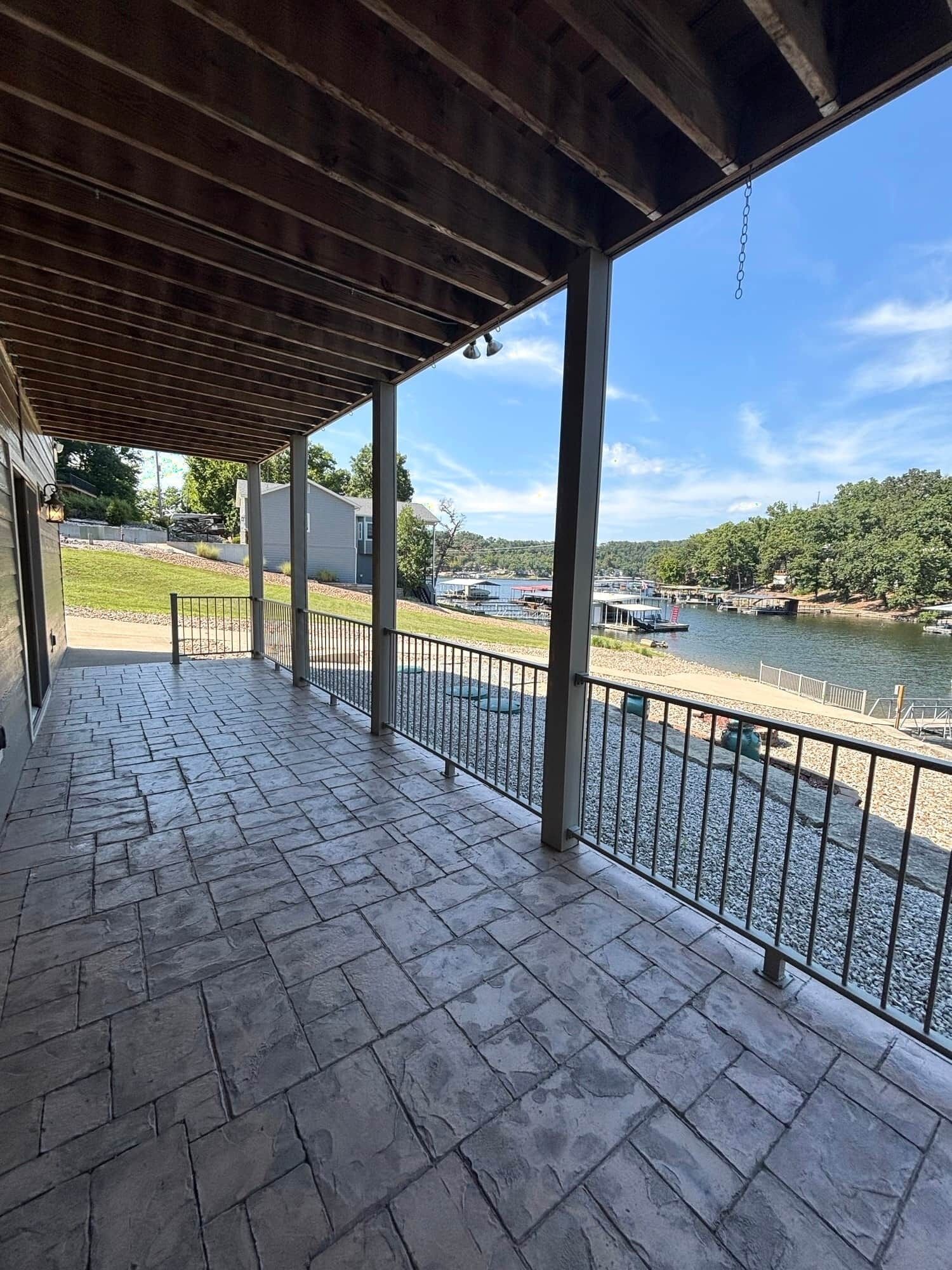 A covered patio with stone flooring and metal railings overlooking a river.