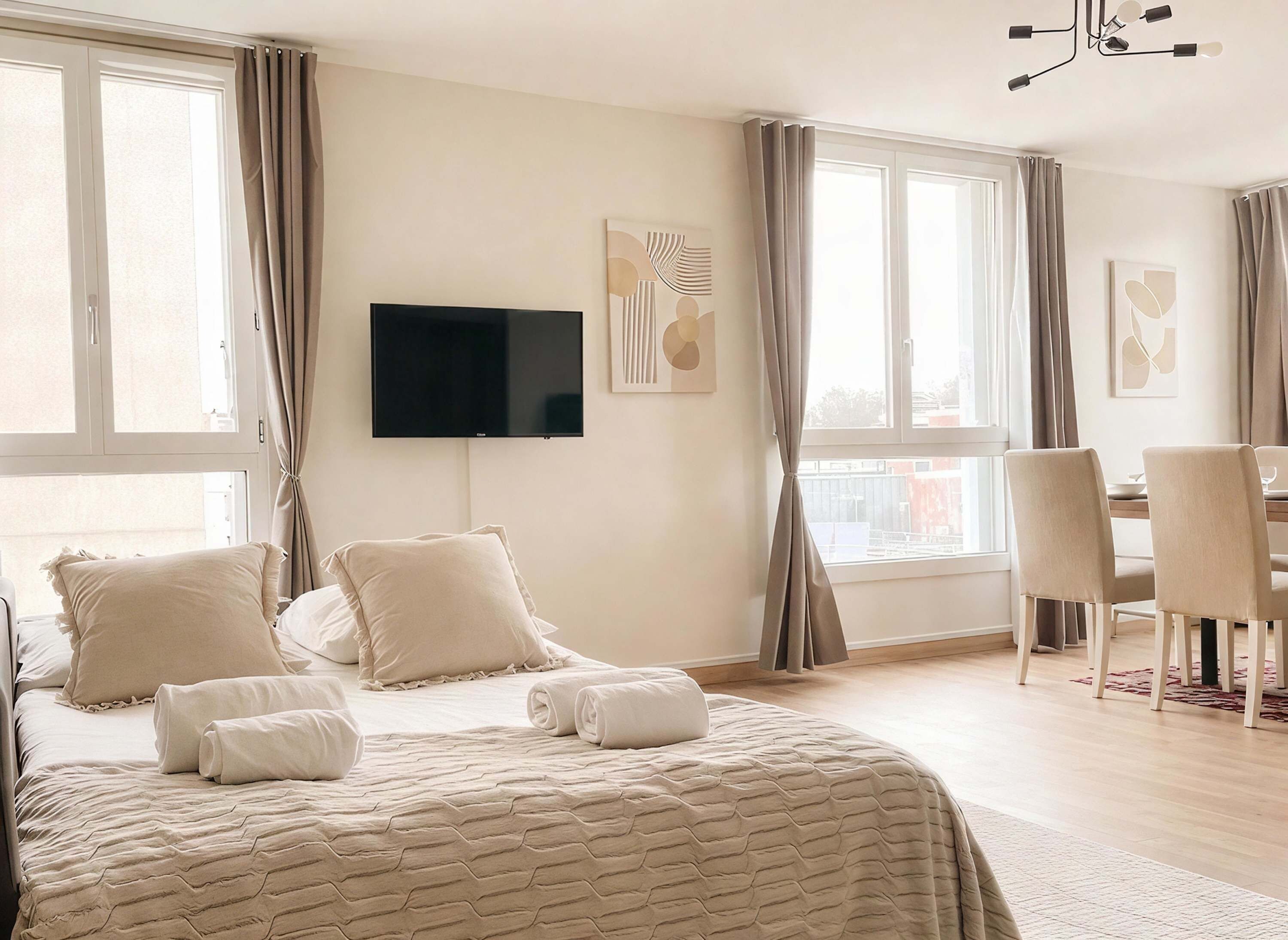 Een hotelkamer met een bed, een flatscreen televisie, een zithoek met stoelen en grote ramen met gordijnen.
