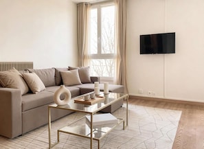 Una sala de estar moderna con un sofá, una mesa de centro de vidrio y un televisor de pantalla plana montado en la pared.