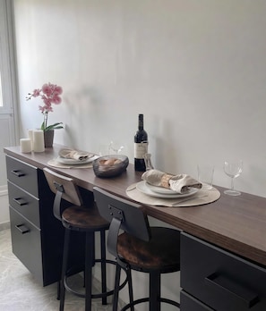 Un comedor con una mesa de madera dispuesta para dos personas, una botella de vino y una orquídea en maceta.