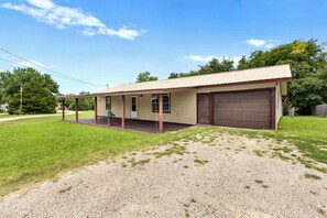 A single-story building with a covered porch, a garage, and a gravel driveway. - 3-bedroom house in peaceful Checotah right of 69 Highway. (Checotah)