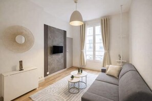 Ein modernes Wohnzimmer mit einer Couch, einem an der Wand montierten Fernseher, einem runden Spiegel und einem Fenster mit Vorhängen.