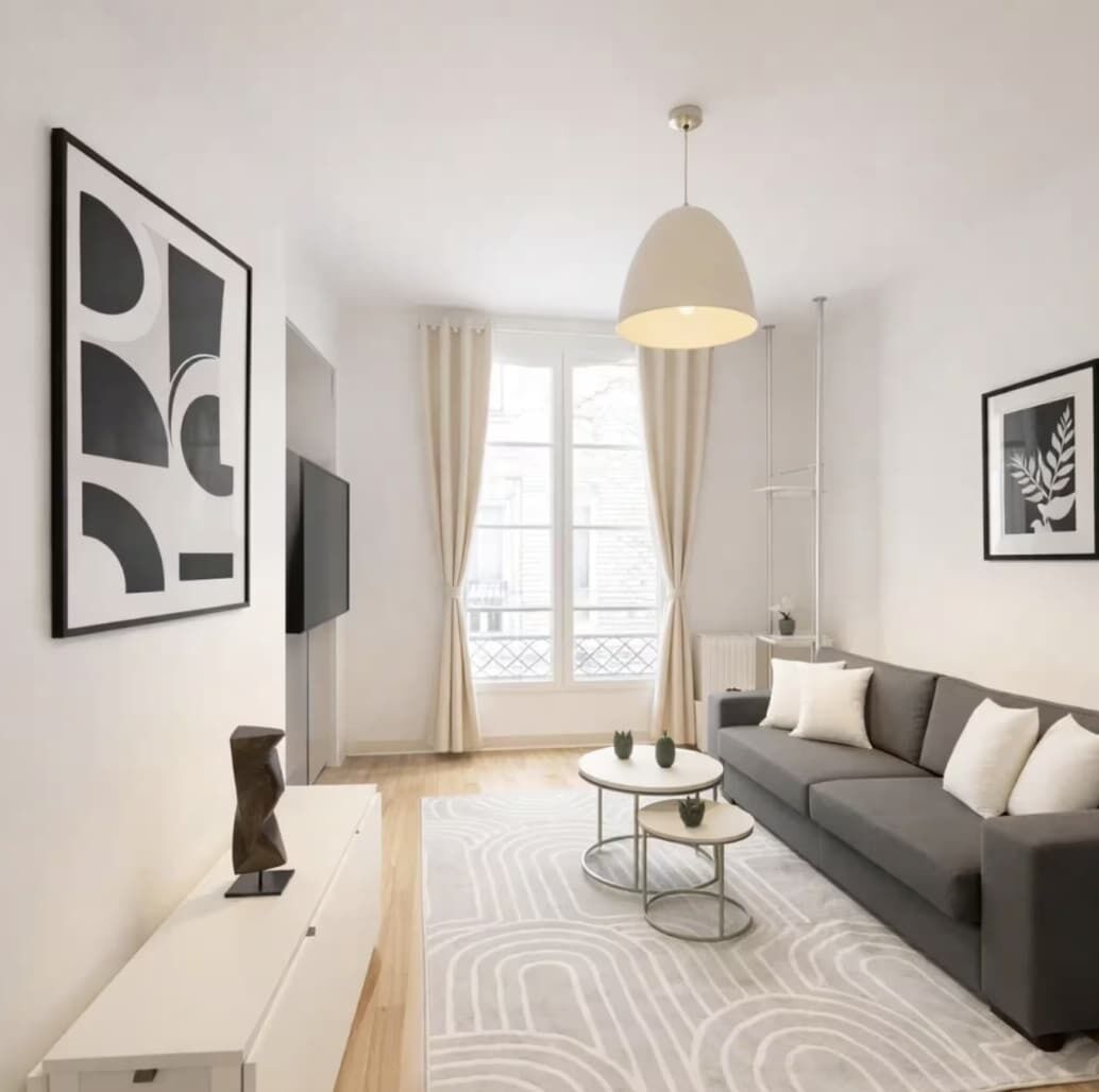 A modern living room with a grey sofa, white cushions, a round coffee table, and abstract wall art.