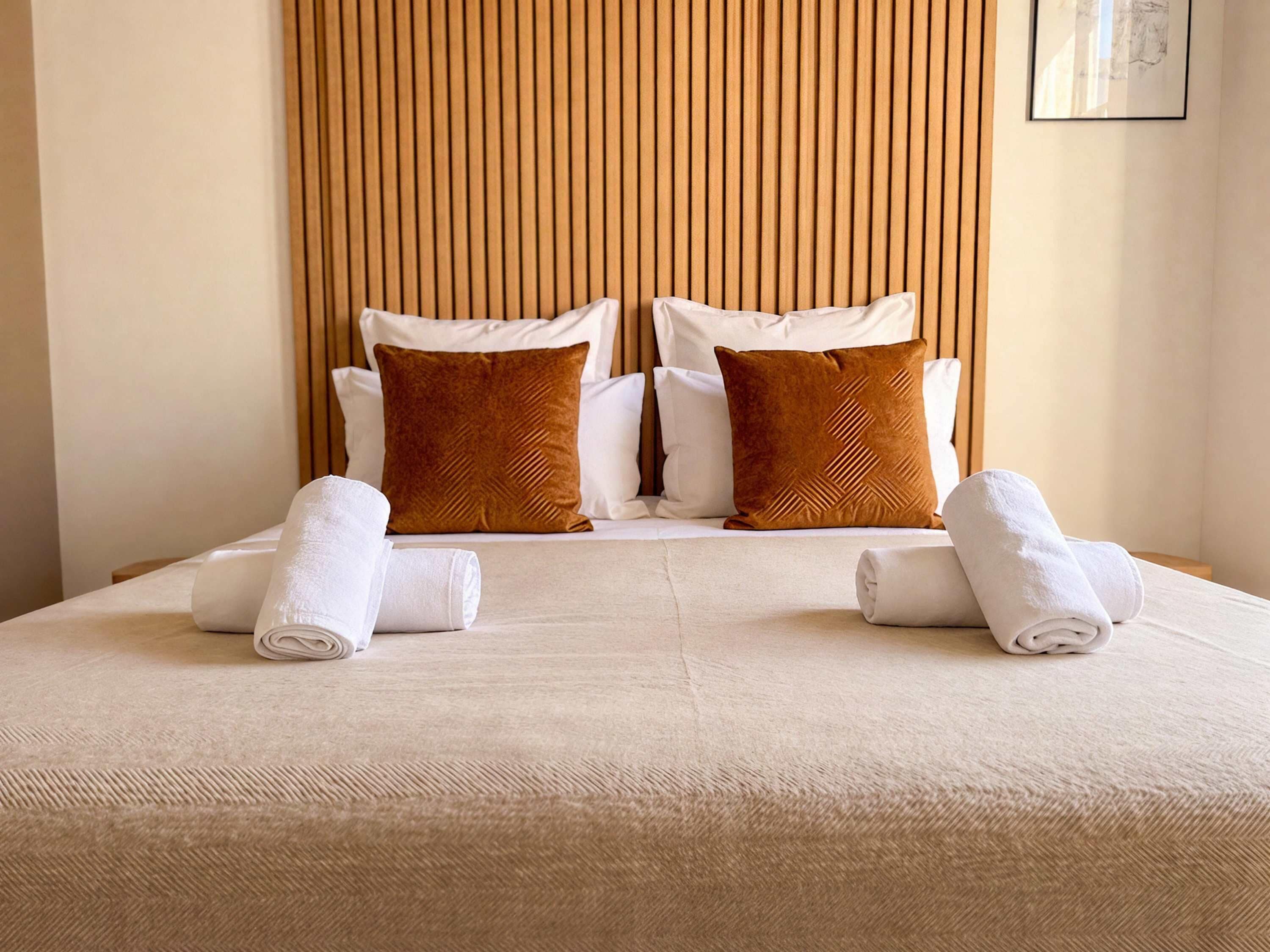 Una cama doble con dos almohadas y dos toallas enrolladas.