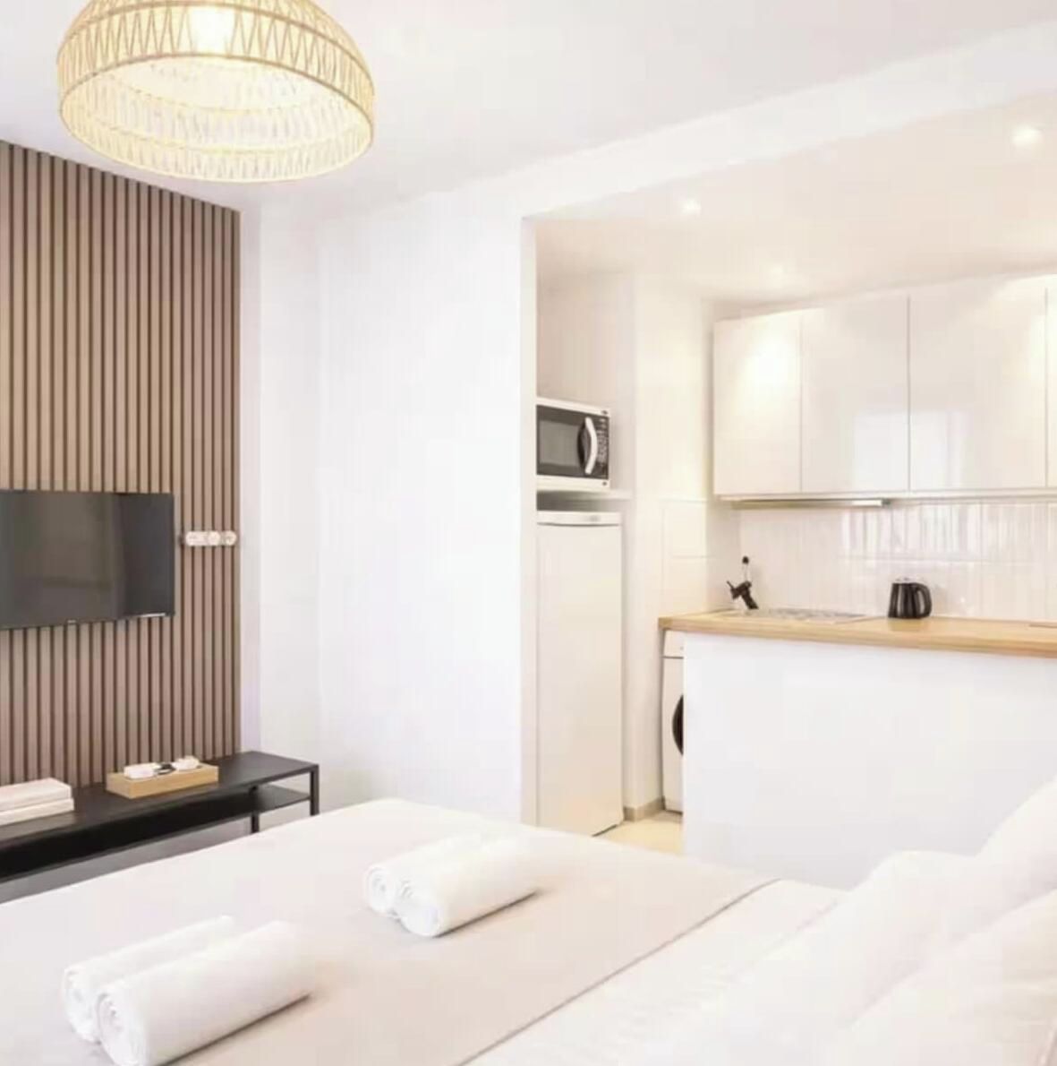 Een hotelkamer met een bed, een flatscreen televisie aan de wand, een wandpaneel van hout, een kitchenette met een magnetron en een koffieapparaat.