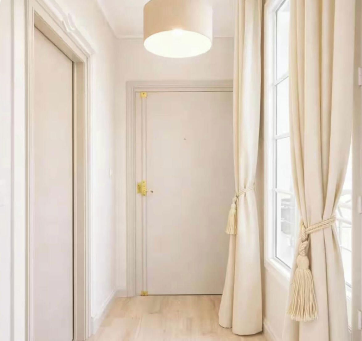 A hallway with a closed door, a light fixture, and a window with curtains.
