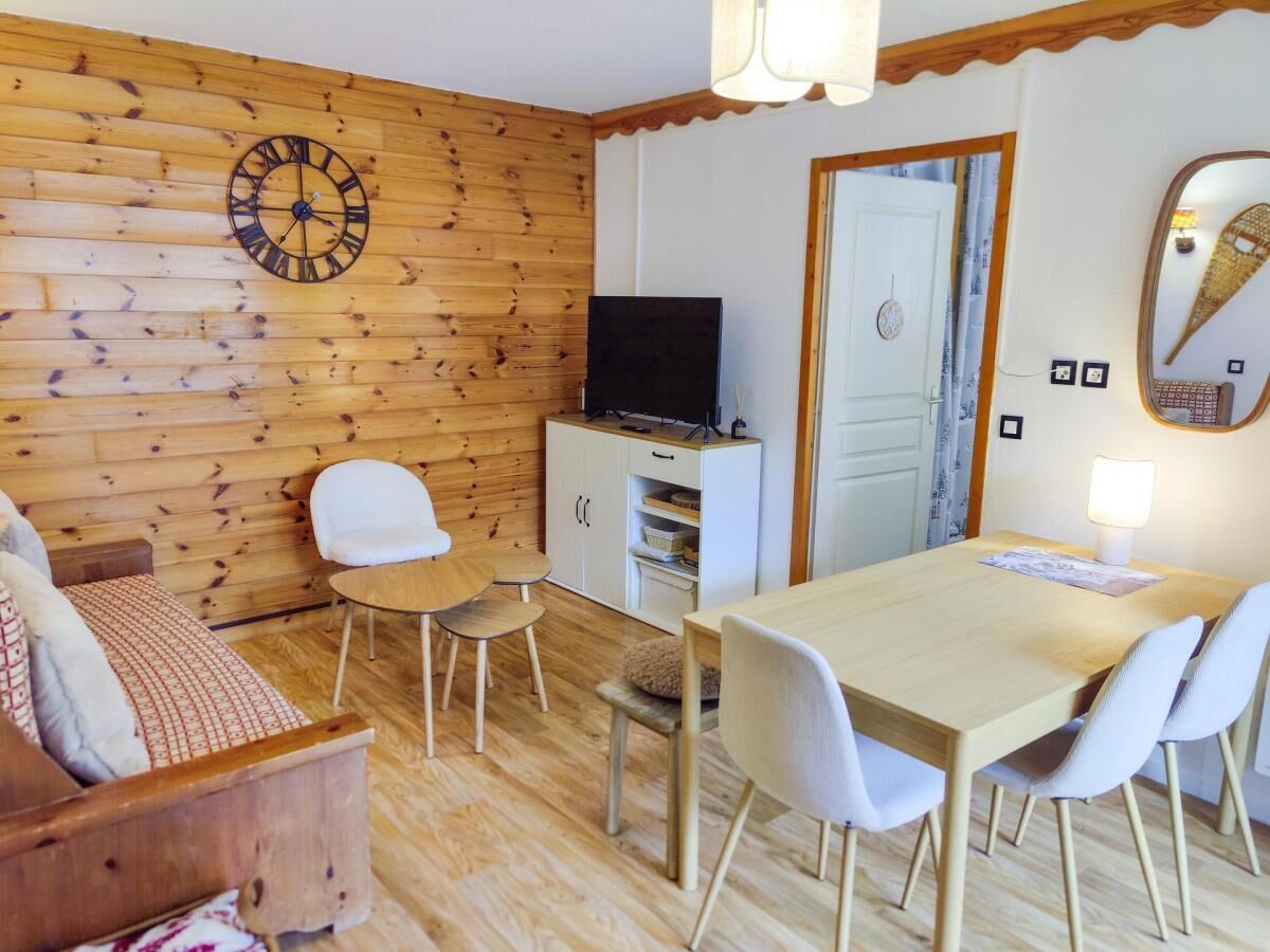 A cozy room with a wooden wall, a dartboard, a TV, a dining table with chairs, and a sofa.