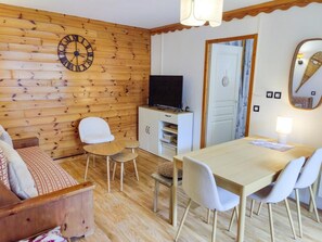 A cozy room with a wooden wall, a dartboard, a TV, a dining table with chairs, and a sofa. - 40m from ski slopes, 1st floor, fitness, swimming pool, sauna, balcony, tv, ski locker, 39m² (Les Orres)