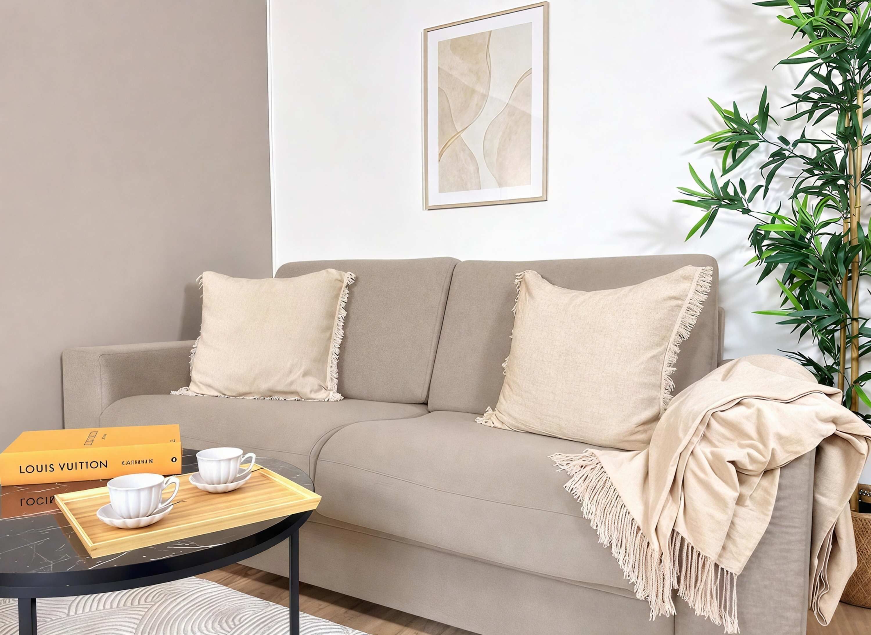 A living room with a sofa, two pillows, a tray with a cup and saucer, a Louis Vuitton box, and a framed abstract painting on the wall.