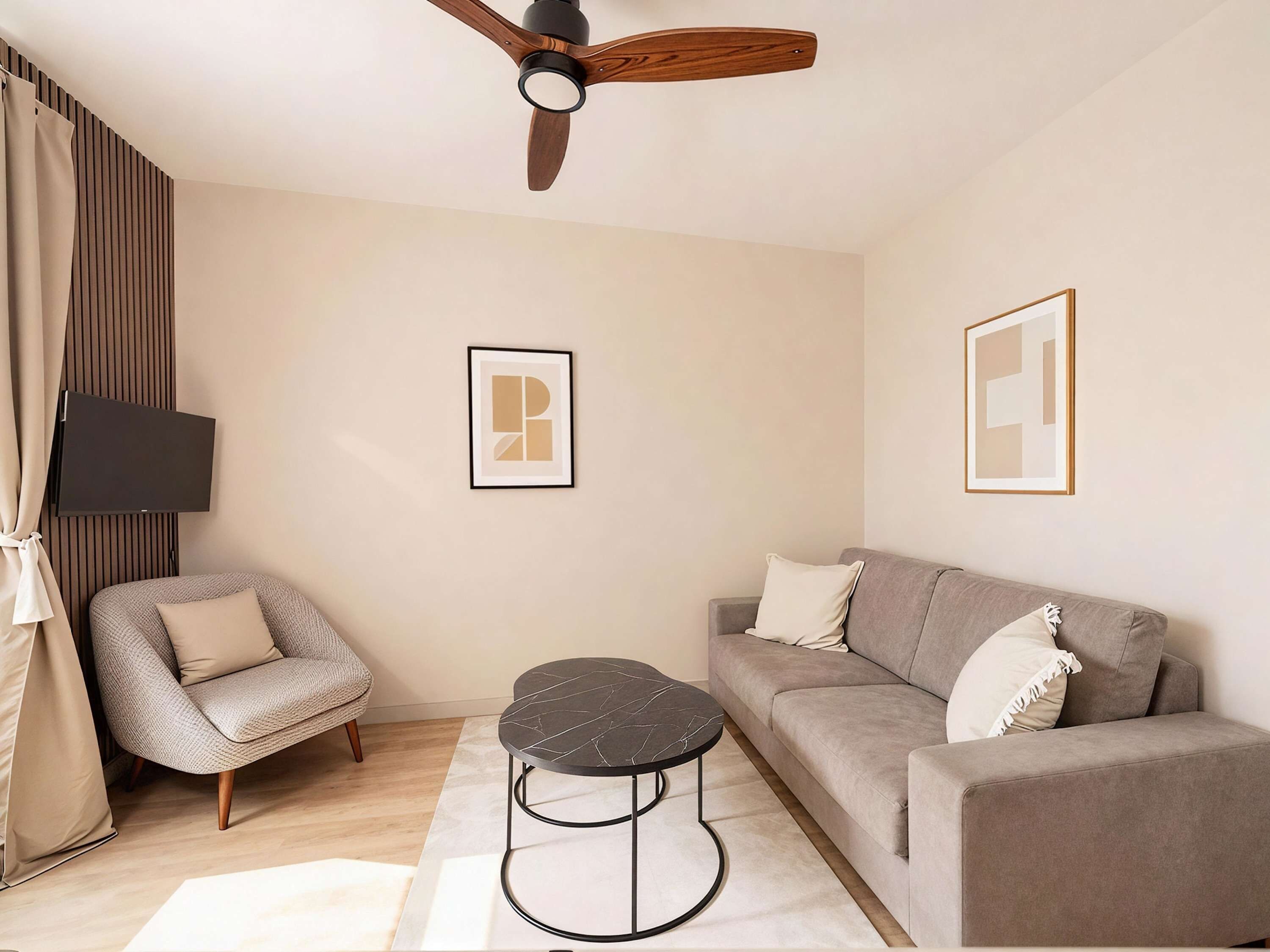 A modern living room with a sofa, armchair, round coffee table, ceiling fan, and wall-mounted TV.