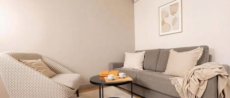A living room with a patterned armchair, a grey sofa, a round coffee table, and a framed abstract artwork on the wall.