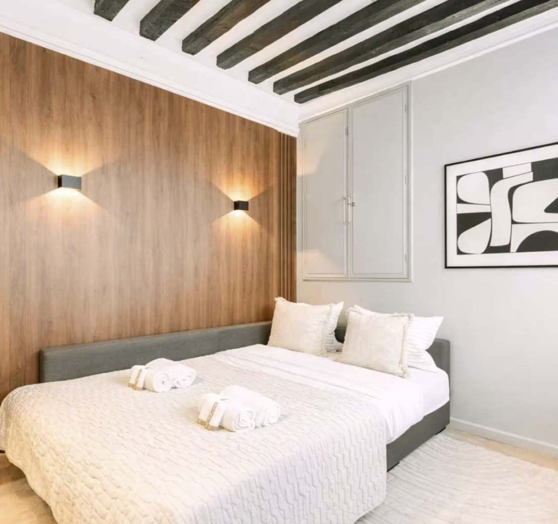 Quarto com cama, duas luzes fixadas na parede, guarda-roupa e uma obra de arte abstrata emoldurada.