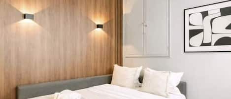 Une chambre à coucher comprenant un lit, deux lampes fixées au mur, une armoire et une œuvre d’art abstraite encadrée.