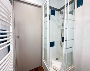 A glass-enclosed shower with a handheld showerhead, a white towel, and toiletries on the floor. - Cozy Studio - Marais, Louvre by Melvane (Paris)