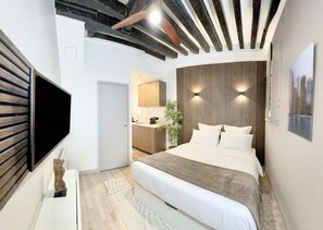 Quarto de hotel moderno com cama, televisão de tela plana, teto de madeira e vista para a cozinha.