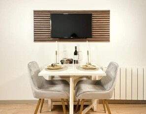 Ein Essbereich mit einem Tisch, zwei Stühlen, einem an der Wand befestigten Fernseher und einem Heizkörper darunter.