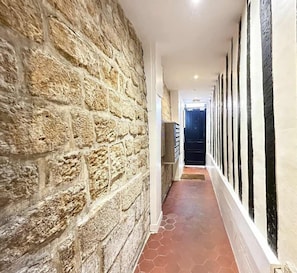 Um corredor com uma parede de pedra de um lado e uma parede branca com listras verticais pretas do outro.