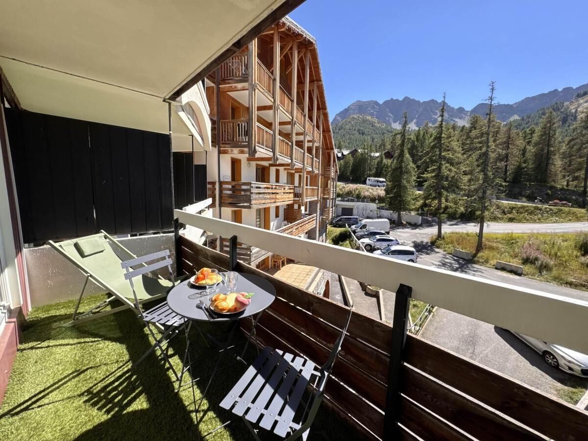 Een balkon met een tafel, stoelen en uitzicht op een berglandschap.