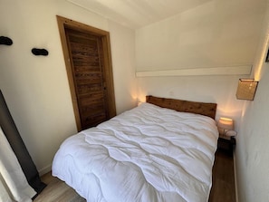 A bedroom with a wooden door, a bed with white bedding, and a bedside lamp. - 100m from ski slopes, 6th floor, balcony, tv, ski locker, 27m², Vars (Vars)