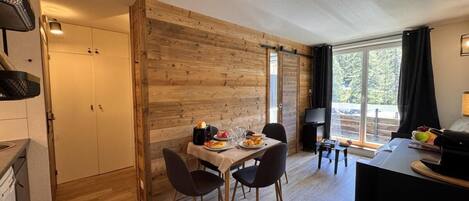 A modern kitchen with wooden walls, a dining table with chairs, and a large window providing natural light.
