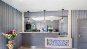 A reception area with a modern design, featuring a reception desk, a decorative vase with flowers, and a tiled accent wall. - Work, Rest & Recharge Near Pasadena l 2 Queen Suite w/ Kitchen (Deer Park)
