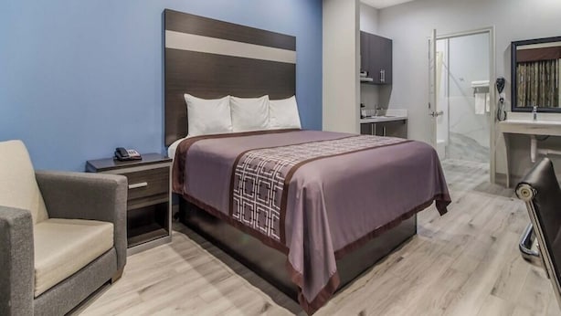 Ein Hotelzimmer mit Bett, Nachttisch, Stuhl und einem Badezimmer mit Dusche und Toilette.