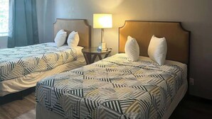A hotel room with two beds, each with a patterned bedspread, a bedside table with a lamp, and a window with curtains. - Pet-Friendly Unit w/ 2 Queen Beds | 12 Min Walk to Frank Phillips College (Borger)