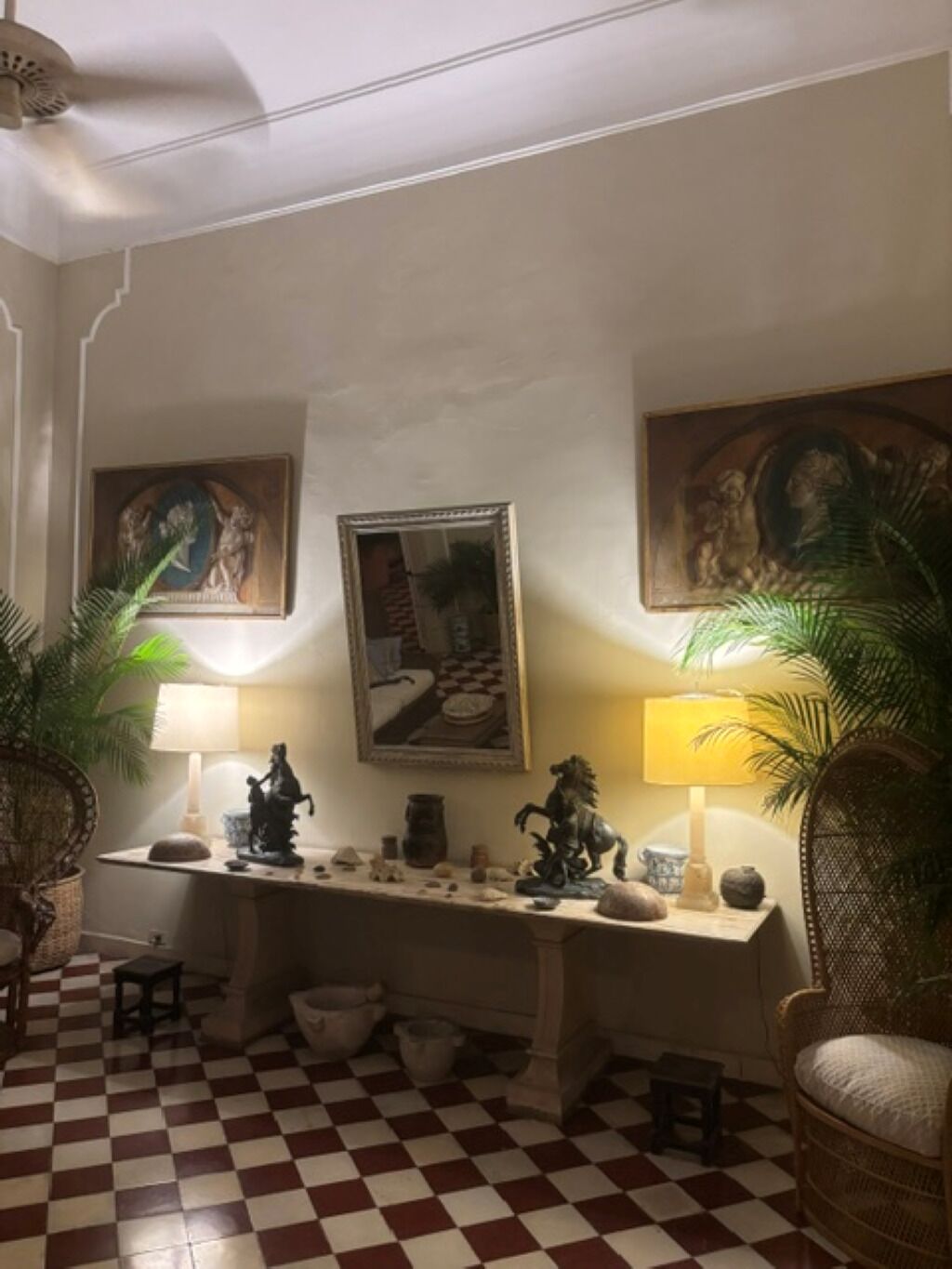 A room with a checkered floor, a desk with decorative items, two lamps, and framed artwork on the walls.
