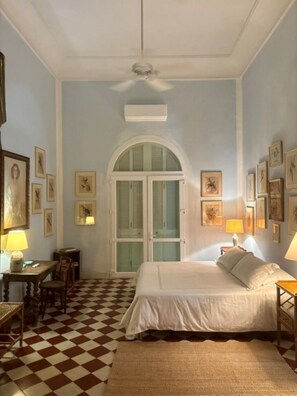 A hotel room with a checkered floor, a bed with white linens, a desk with a lamp, and framed pictures on the walls. - Historic Waterfront Villa with Dock, Private Pool and Caribbean Charm (Cartagena)