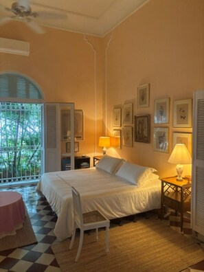 A bedroom with a bed, bedside tables, a chair, a window with shutters, and framed pictures on the wall. - Historic Waterfront Villa with Dock, Private Pool and Caribbean Charm (Cartagena)