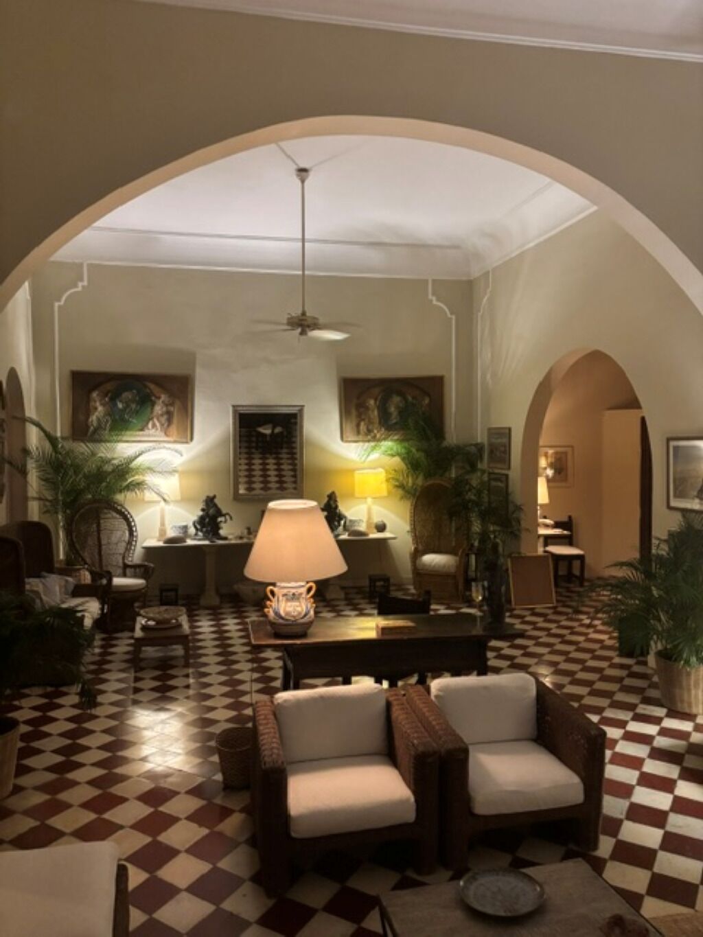 A hotel lobby with a checkered floor, arched ceiling, and a central seating area with lamps.