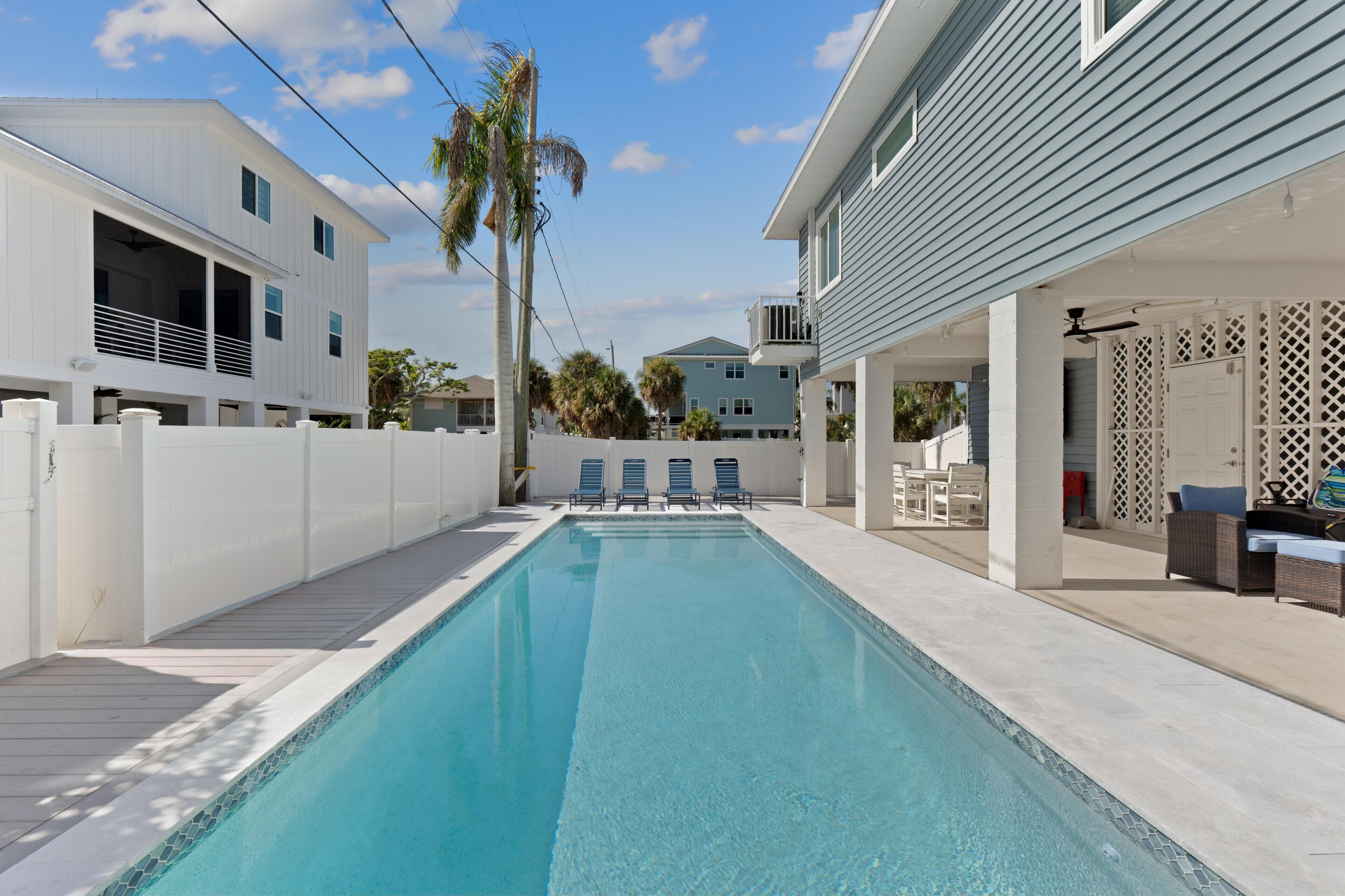 Une piscine avec une terrasse en bois, des chaises longues et un espace patio couvert.